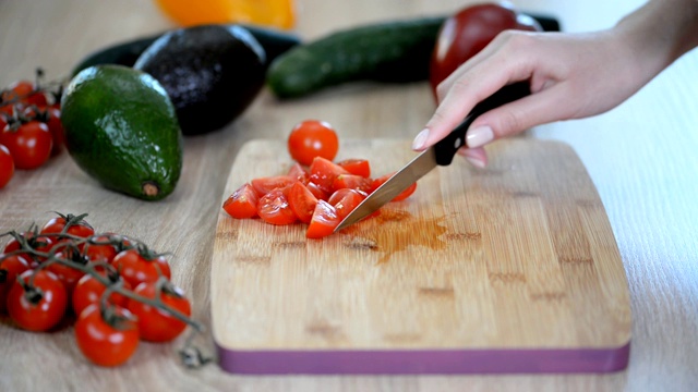 一个女人正在切樱桃西红柿，准备放在木桌上做沙拉。视频下载