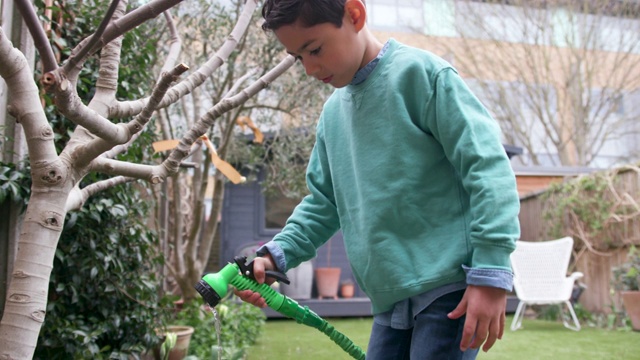小男孩小心翼翼地用软管在花园里浇花视频下载