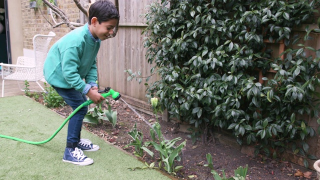 小男孩小心翼翼地用软管在花园里浇花视频素材