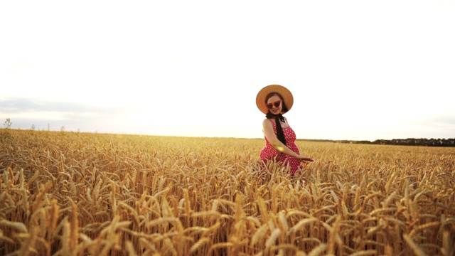 穿着红色裙子和帽子的快乐女人在金色的麦田里旋转，微笑。美丽、自然、旅游、收获、和谐的理念。视频素材