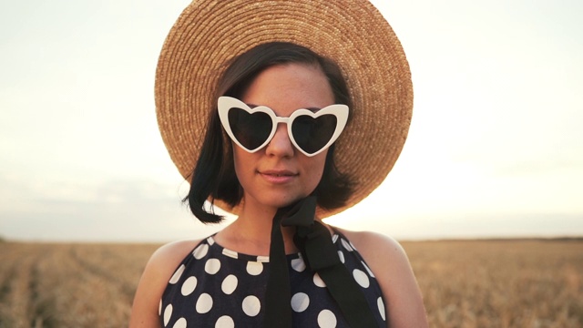 麦田里时髦女人的肖像。传统女孩草帽，心形眼镜，黑色圆点裙子。旅游、时尚、自然理念视频素材