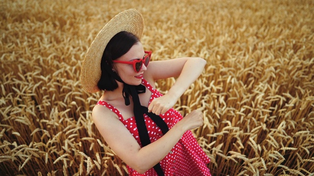 漂亮有趣的女孩穿着红色的衣服和草帽在金色的麦田里跳舞。成功，复古风格，快乐，幸福理念视频素材