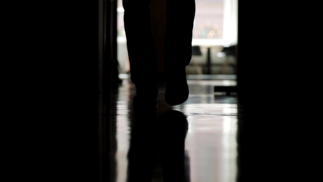 慢镜头中，一名男子的双腿沿着办公室走廊向打开的办公室门走去，背影剪影视频素材