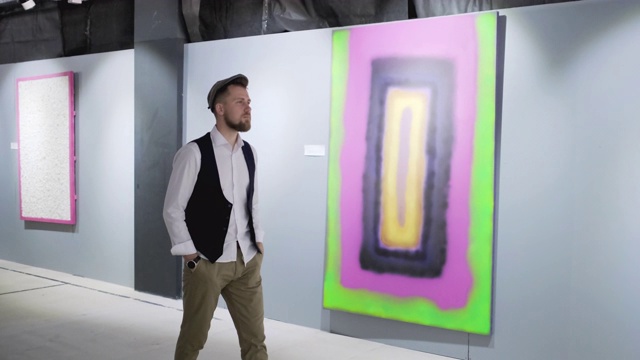 一名男性艺术爱好者在画廊大厅里漫步，欣赏绘画视频素材