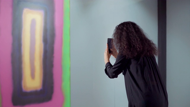 一位黑发女子正在用智能手机拍摄一幅抽象画视频素材