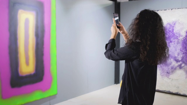 一个黑发女孩正在美术馆的大厅里用手机拍摄现代照片视频素材