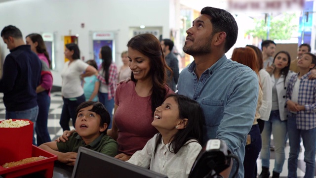 快乐的拉丁美洲年轻夫妇和他们的孩子在电影院的小卖部选择小吃视频素材