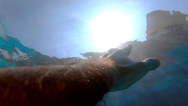 手臂请求帮助，试图触及太阳。人在海洋中溺水或漂浮到海面的观点。男性的手从水中伸展到阳光下。慢镜头观点视频素材