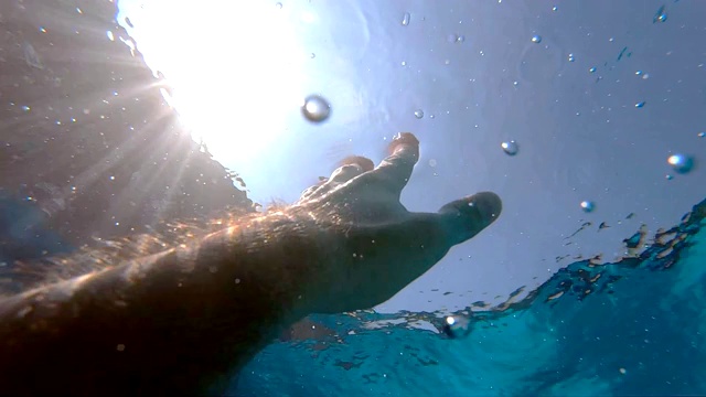 手臂请求帮助，试图触及太阳。人在海洋中溺水或漂浮到海面的观点。男性的手从水中伸展到阳光下。慢镜头观点视频素材