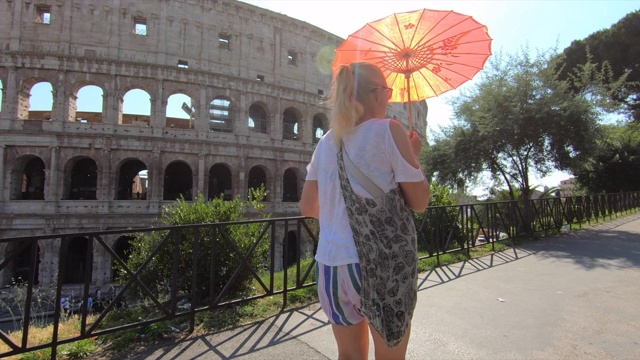在欧洲的意大利罗马，一位女士打着遮阳伞走过圆形大剧场。——慢动作视频素材