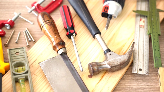 从俯视图拍摄:木制工匠的工作工具，如锤子，防护手套，水平仪，无绳螺丝刀钻和刀视频下载