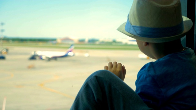 近距离看飞机的小孩。一个男孩坐在那里看着机场的跑道。视频下载