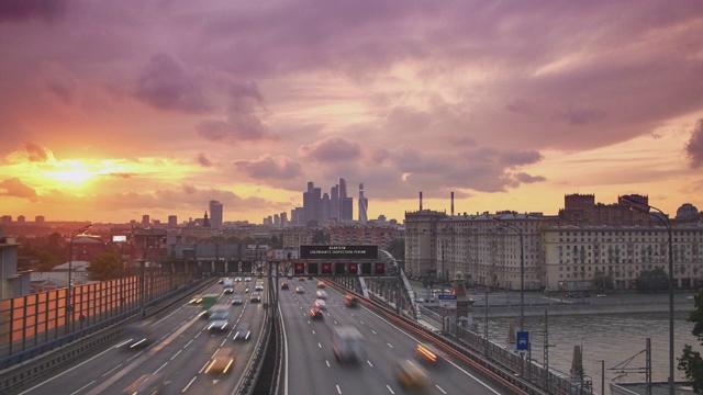 城市景观与密集的交通在宽阔的城市高速公路在前景和办公室摩天大楼在日落的背景视频素材