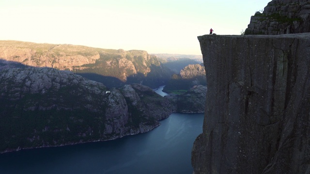 封锁:人们在高高的悬崖上欣赏风景，阳光覆盖了部分地区-布道石，挪威视频下载