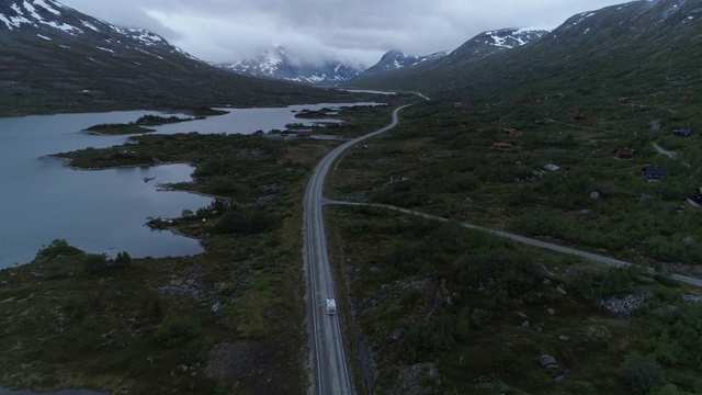 航拍:冬季，在挪威盖兰格峡湾，无人机在沿着通向山脉的湖的高速公路上接近露营车视频素材