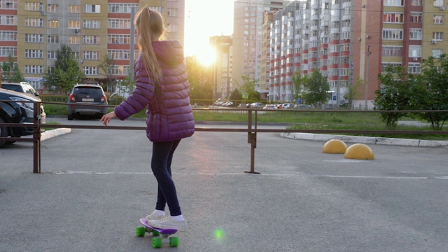 少女滑板在城市街道上的长板黄昏日落。年轻的女孩在街道上玩滑板，阳光穿过住宅楼。运动的生活方式。视频素材