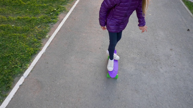 年轻的滑板女孩骑在滑板在城市的慢镜头，从上面看。少女喜欢在城市街道上玩长板滑板。极端的青年运动。视频素材