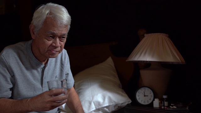 一个抑郁的老年人坐在床上，由于失眠和服药而无法入睡视频素材
