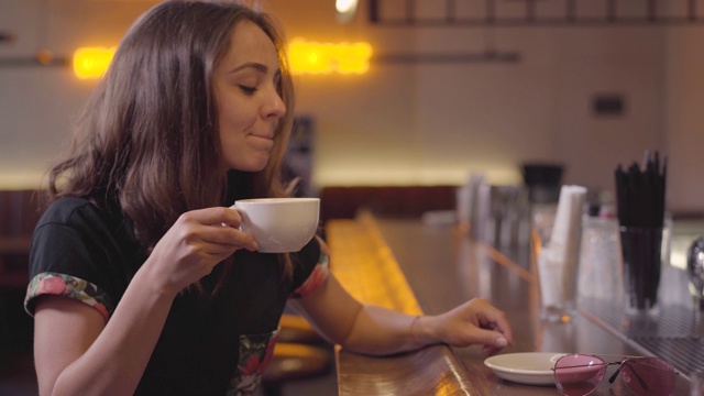 肖像的魅力年轻女子享受她的咖啡坐在吧台。视频下载