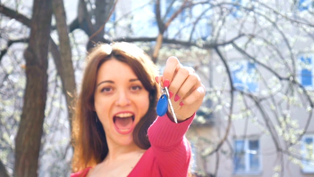 年轻兴奋的女孩显示钥匙从新的房地产与蓝色的钥匙链，女性手与红色美甲在户外在城市的背景春天。视频素材