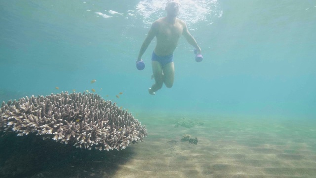 人们在水下用哑铃训练看珊瑚和鱼，坐在沙滩上。视频下载