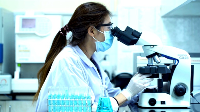 穿着白色防护服的女科学家用吸管将化学物质注入试管并在实验室进行科学实验时观察显微镜- 4K视频下载
