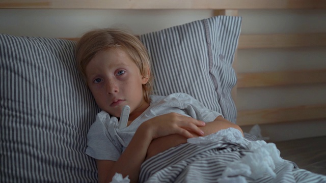 一个生病的小男孩拿着体温计躺在床上的超慢速镜头。婴儿流感概念视频素材