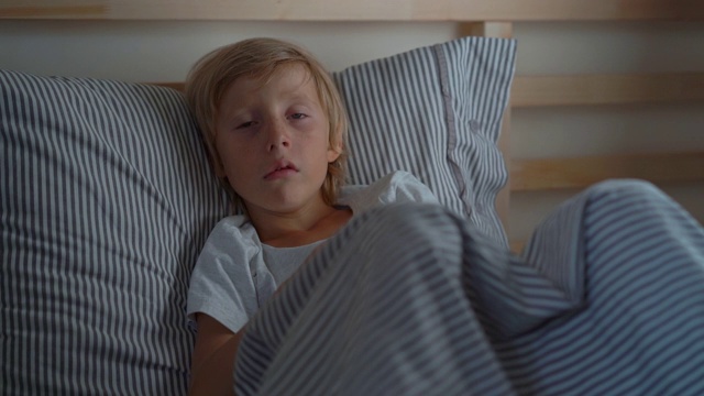 一个男孩用餐巾擦鼻涕的超慢速镜头。生病的小男孩躺在床上。婴儿流感概念视频素材
