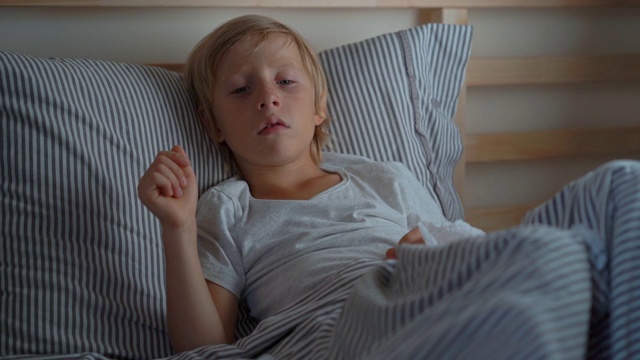 生病的小男孩躺在床上。一个男孩在床上咳嗽的超慢速镜头。婴儿流感概念视频素材