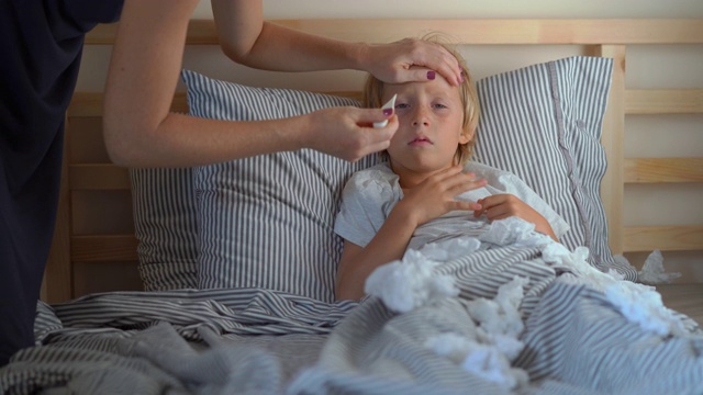 一个生病的小男孩躺在床上。母亲用精油软膏擦男孩的胸部，并测量他的体温。婴儿流感概念视频素材