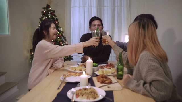 一群亚洲朋友在圣诞晚宴上欢声笑语。快乐的泰国人在一起玩有趣的谈话和晚餐派对。快乐的泰国人一起吃披萨在派对期间在家。慢动作的场景视频购买