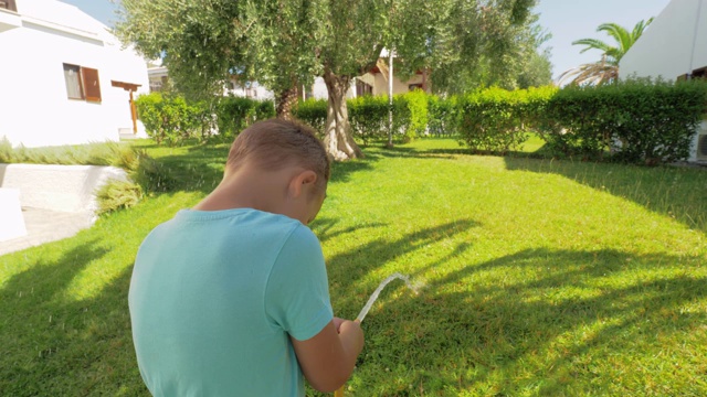 顽皮的孩子在房子旁边的草坪上浇水视频素材