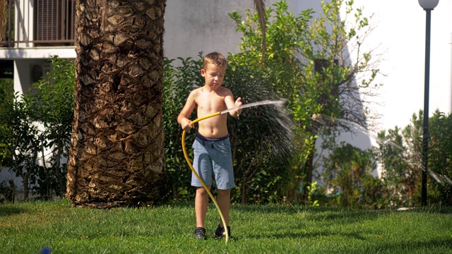男孩试图应付水射流时，给草坪浇水视频素材