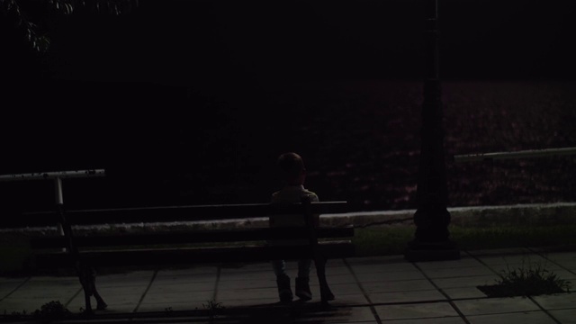 孤独的孩子晚上坐在户外的长椅上视频素材