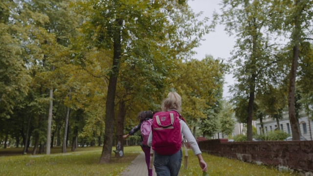 两个背着背包的朋友去上学。在公园里散步的混合种族学校的孩子的后视图。慢动作镜头视频素材