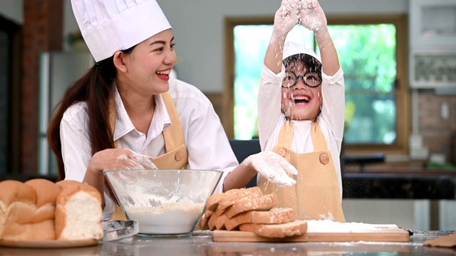 可爱的亚洲小男孩和美丽的母亲在家庭厨房的桌子上筛选生面团面粉准备烘焙和蛋糕。泰国小孩像厨师一样玩面粉。幸福家庭生活理念视频素材