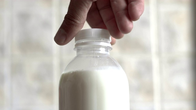 男性的手旋转着牛奶的瓶盖。视频下载