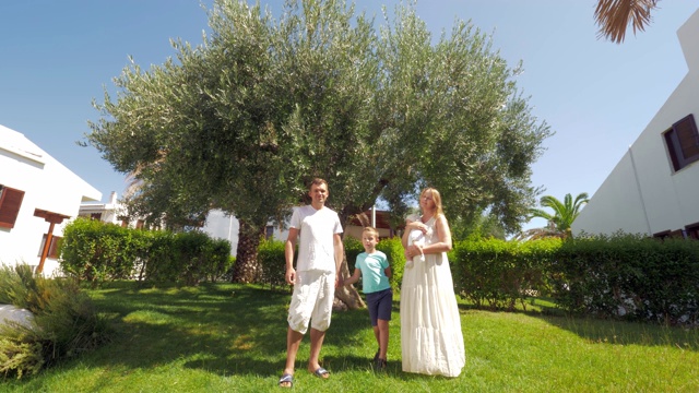 一个年轻的家庭和两个孩子在花园里的橄榄树附近视频下载