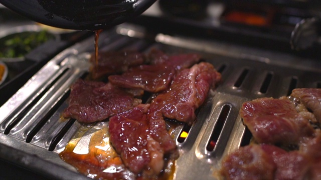 新鲜的牛肉被倒在热气腾腾的韩国烧烤架上视频下载