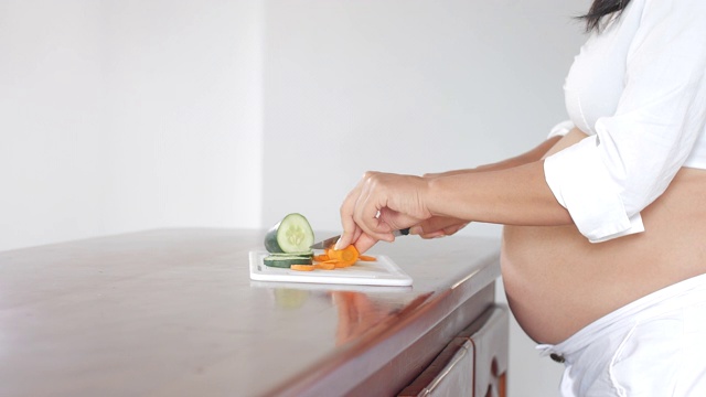 一名拉丁美洲孕妇站在厨房的木质柜台前切蔬菜视频素材