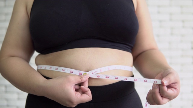 一个超重的女人在量她的肚子视频素材