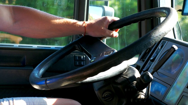 靠近男性司机的手握着方向盘和驾驶他的卡车在乡村道路上。一个人控制着他的卡车驶向目的地。货车车厢内的景象。慢动作视频下载