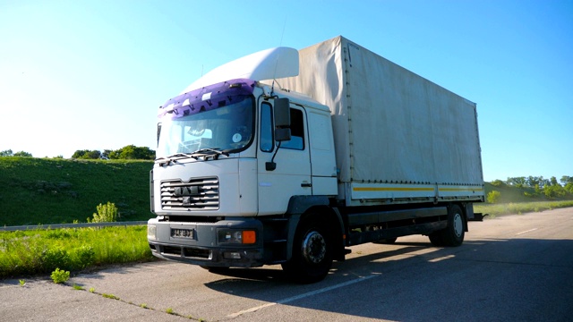 摄像机跟随卡车与货物拖车在公路上行驶和运输货物。在阳光明媚的日子里，一辆卡车在乡间公路上行驶。货物运输的概念。慢镜头视频素材