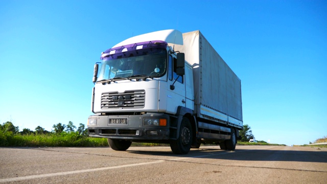 低视野的卡车与货物拖车在公路上行驶和运输货物。在阳光明媚的日子里，一辆卡车在乡间行驶。背景是美丽的蓝天。慢镜头视频下载