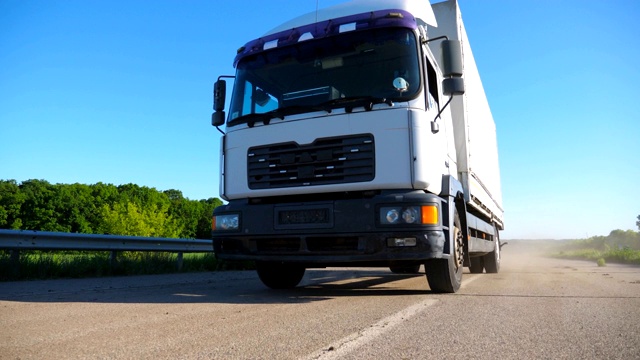 低视野的卡车与货物拖车在公路上行驶和运输货物。在阳光明媚的日子里，一辆卡车在乡间行驶。美丽的背景。慢镜头视频下载