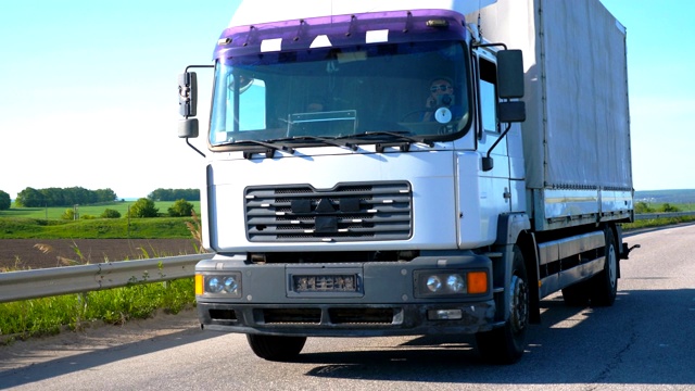在夏季的日子里，镜头跟随卡车和货运拖车在高速公路上行驶，运送货物。以自然景观为背景的卡车穿越乡村。慢动作前视图特写视频素材
