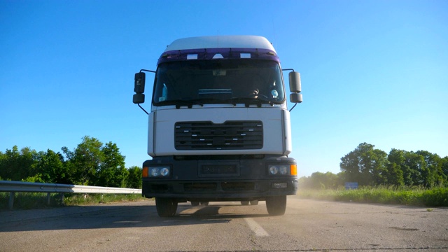 卡车正面视图与货物拖车行驶在公路上运输货物在夏季的一天。白色的卡车驶过乡村，背景是美丽的风景。慢镜头视频素材