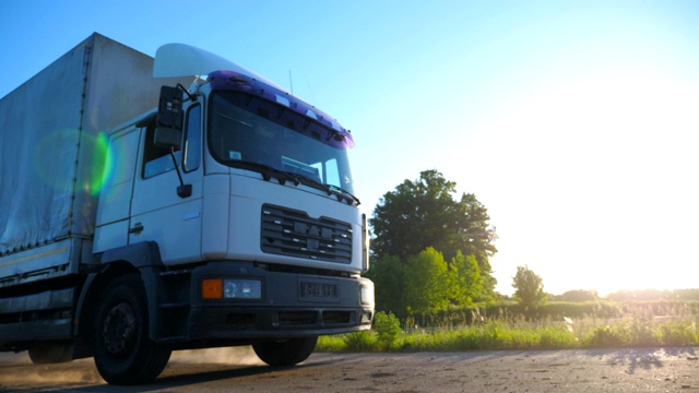 在日落时分行驶在高速公路上运送货物的带有拖车的卡车。卡车在美丽的自然环境中穿过乡村公路。货物运输的概念。慢镜头视频下载