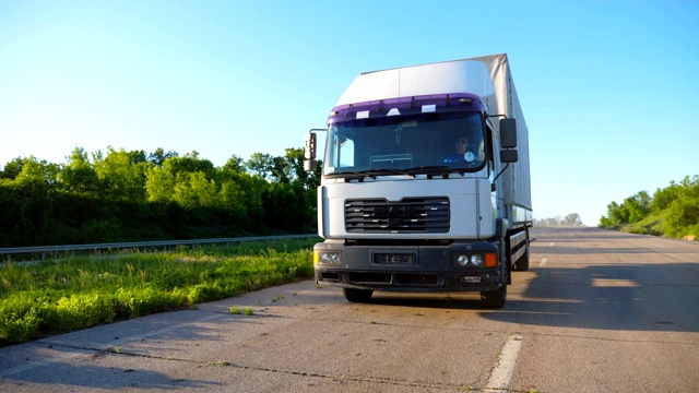 在阳光明媚的日子里，在高速公路上行驶的卡车与货物拖车的正面视图。卡车在乡间公路上行驶。美丽的自然背景。物流的概念。慢镜头视频素材