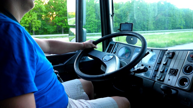 一个面目全非的司机坐在他的卡车的方向盘后面，在乡下兜风。男人开车去目的地运送货物。关闭卡车的方向盘和仪表盘。慢动作视频下载